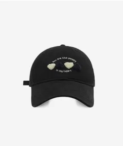 Detail view of black baseball cap featuring embroidered heart graphics and cute text design.