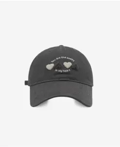Close-up detail of the grey baseball cap featuring cute fluffy heart embroidery and text.