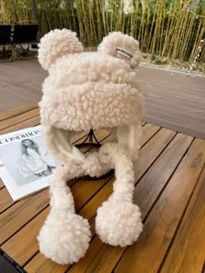 Vue détaillée du bonnet en polaire beige avec oreilles d'ours et pompons duveteux chauds.