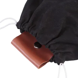 Vue détaillée de la poche de cueillette en toile, tissu noir et rabat en cuir marron, bouton pression.