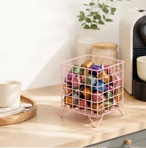 Detailed view of the pink metal wire coffee capsule storage basket on a wooden tabletop.