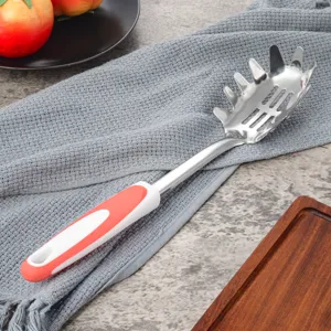 Dettaglio primo piano cucchiaio per spaghetti in acciaio inox, manico rosso bianco antiscivolo.