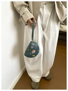 Detailaufnahme der Halbmond-Handgelenktasche mit filigranem Blumenstickmuster und Trageriemen.