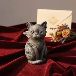 Dettaglio statua gatto memoriale in resina, ornamento angelo inciso su tessuto rosso.
