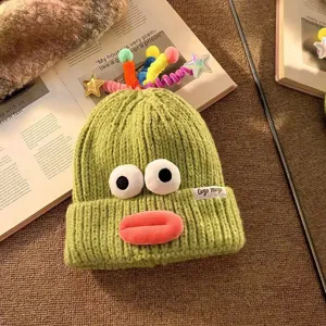 Detailansicht einer lustigen grünen Strickmütze mit süßen Augen und bunten Plüsch-Details.
