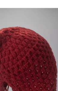 Close-up detail of a dark red knitted hollow beanie cap with tassel texture, soft knit.
