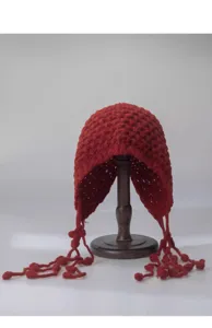 Red knitted hollow out bonnet hat detail, close up view of wool crochet tassel ball design.