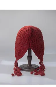 Red knitted hollow beanie hat with tassel earflaps, autumn winter wool cap detail view.