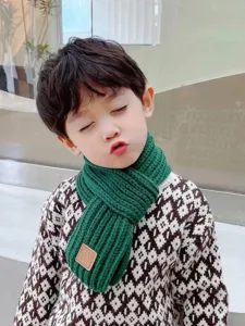 Close-up detail of children's green knitted scarf with leather tag, cozy winter accessory.