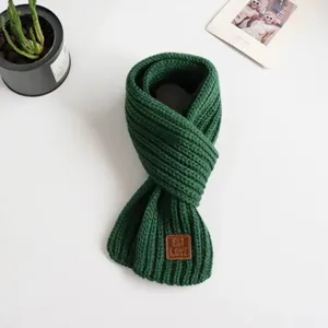 Dark green knitted scarf detail shot showing ribbed texture and cute brown leather patch tag.
