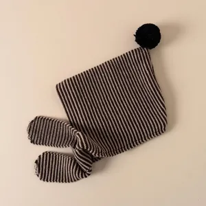 Close-up detail of cozy striped knit baby hat with ear flaps and black pom-pom decoration.
