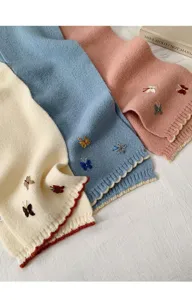 Close-up detail of knitted winter scarf with embroidered butterflies and contrast wave edge.