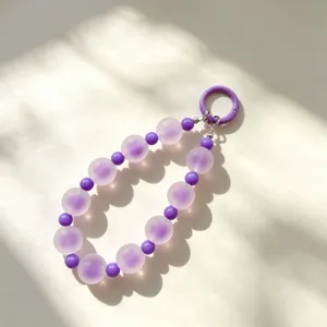 Dettaglio del cinturino per telefono con perline viola opache e lucide con chiusura ad anello.