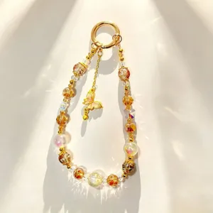 Exquisite crystal beaded phone chain detail, luxury gold butterfly charm and gold foil beads.