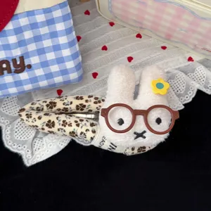 Cute plush rabbit hair clip with floral fabric wrap and round glasses detail, soft accessory.