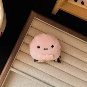 Close-up detail shot of a cute pink plush animal hair clip displayed on a soft beige tray.
