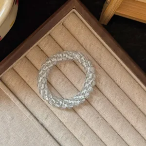 Detail shot of transparent telephone wire hair tie on beige display tray, clear and durable.