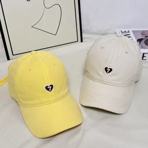 Close-up of retro baseball caps with heart embroidery in yellow and beige, lifestyle scene.