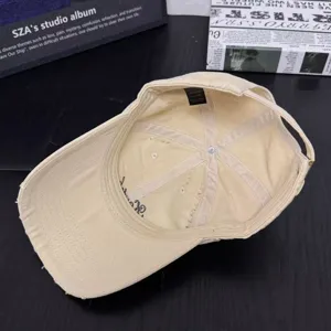 Detailed view of beige distressed cotton baseball cap with adjustable strap and eyelets.
