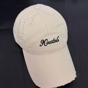 Close-up view of the beige cotton distressed baseball cap featuring black embroidery.