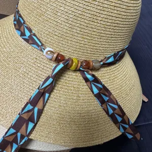 Close-up detail of the stylish straw sun hat featuring geometric ribbon and natural beads.