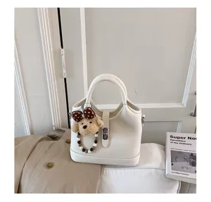 Close-up view of white leather bucket bag featuring metal lock closure and cute bear pendant.
