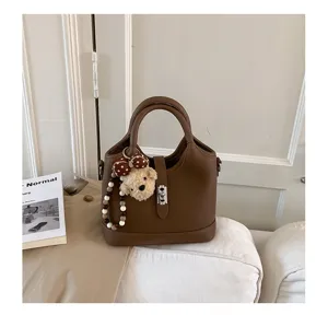 Detail view of brown leather bucket bag with cute bear pendant and metal lock closure on sofa.