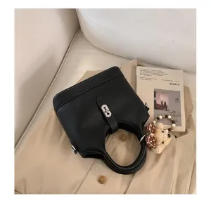 Close-up detail of a black leather bucket bag with metallic clasp and cute bear charm.