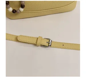 Close-up detail of yellow leather handbag strap with metal buckle and beads, elegant style.