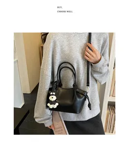 Vue détaillée d'un sac à main noir minimaliste avec pendentif chien et bandoulière élégante.