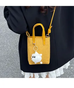 Detailansicht der stilvollen gelben Stroh-Mini-Eimer Tasche mit einem süßen flauschigen Anhänger.