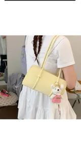 Minimalist yellow shoulder bag detail shot featuring double straps and cute plush bear keychain.