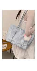 Light blue tote bag detail showing patent leather texture, metal buckles and fluffy plush charm.