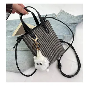 Mini gewebte Umhängetasche für Handys mit schwarzen Ledergriffen und süßem Plüsch-Anhänger.