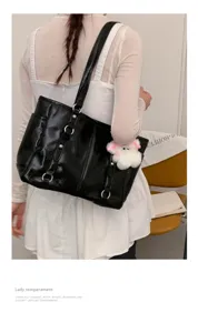 Glossy black shoulder tote bag detail showing metal ring accents and cute plush charm hanging.
