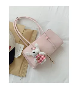 Detail view of pink shoulder bag with cute white plush bunny keychain and checkered dress.
