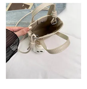 Detailansicht der kleinen beigen Eimer-Tasche mit Henkeln und süßem Plüsch-Anhänger.
