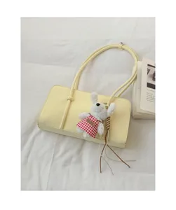 Detail shot of minimalist yellow shoulder bag with cute rabbit plush charm and book prop on fabric.