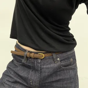Vista detallada del cinturón fino de ante marrón usado con jeans vaqueros, accesorio elegante.