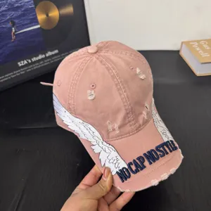 Pink distressed baseball cap with embroidered wings and stylish text detail for daily wear.