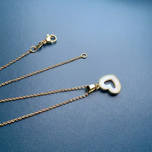 Detailed close-up of a delicate gold chain necklace featuring a white mother of pearl heart pendant.