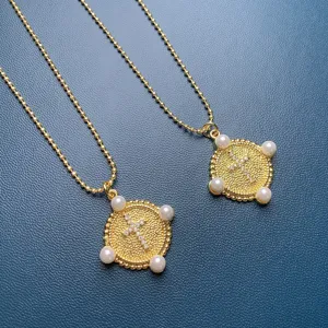 Close-up detail of gold bead chain necklace with rhinestone cross coin pendant and pearls.