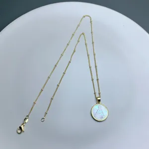 Detalle de un collar de cadena dorada delicada con un colgante redondo de madreperla Virgen María.