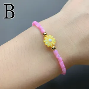 Pink beaded bracelet with yellow daisy charm and gold beads, elegant floral wrist jewelry detail.