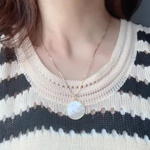 Close-up detail of a delicate gold chain necklace featuring a round white mother-of-pearl pendant.
