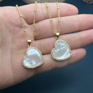 Primo piano di eleganti collane con ciondolo a cuore in madreperla bianca e catenine dorate.