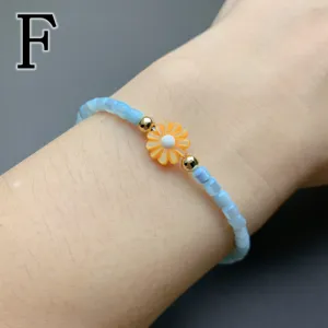 Close-up of the delicate beaded bracelet featuring an orange shell daisy charm and gold beads.