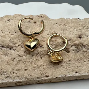 Detalle de pendientes de aro dorados con colgante de corazón sobre fondo de piedra texturizada.