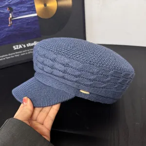 Close-up of a blue knitted bakerboy hat with textured pattern and a chic metal side tag.