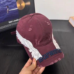 Distressed burgundy baseball cap detail, featuring white embroidered wings and front letter text.